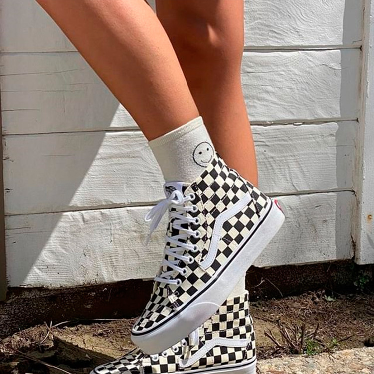 A girl wearing some of the white and black Vans vegan trainers with a smiley face on her socks