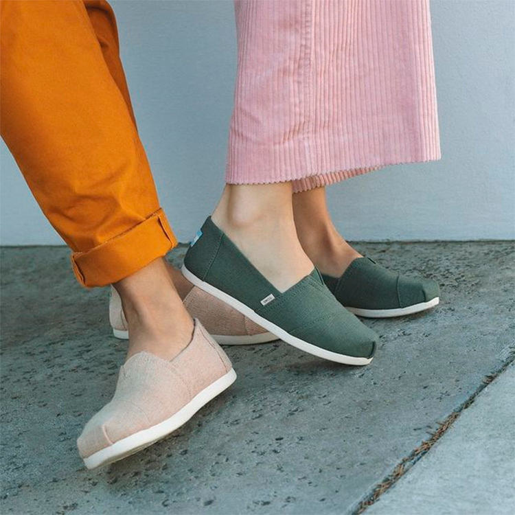 Two people wearing TOMS vegan trainers, one in beige and the other one green